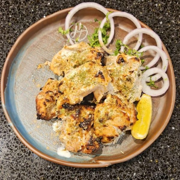 Mausam Indian Flavors' chicken tikka with onion rings, cilantro, and a lemon wedge on a plate.