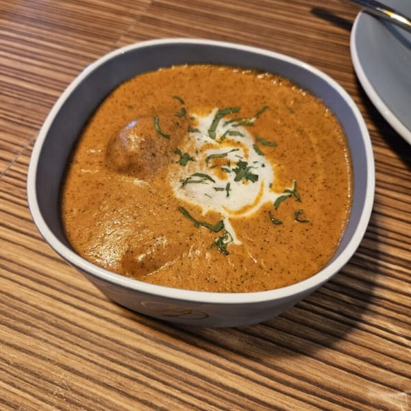 A bowl of Mausam Indian Flavors' butter chicken, garnished with cream and fresh herbs.
