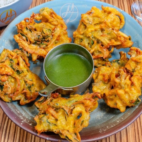 Golden-fried Indian pakoras, crispy and savory, served on a blue plate with a vibrant green dipping sauce.
