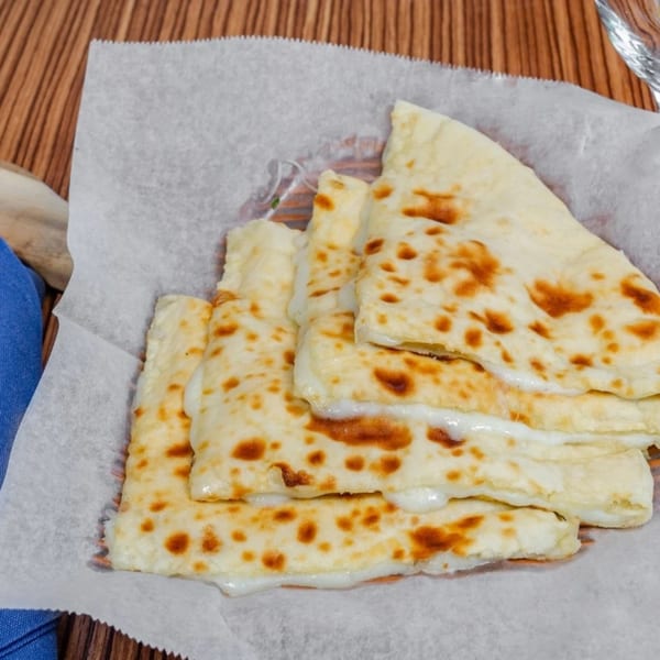 Golden-brown cheese naan bread, cut into triangles, served on white parchment paper.
