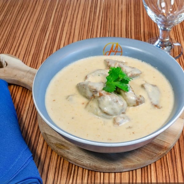 Mausam Indian Flavors' creamy chicken curry with cilantro in a blue bowl on a wooden board.