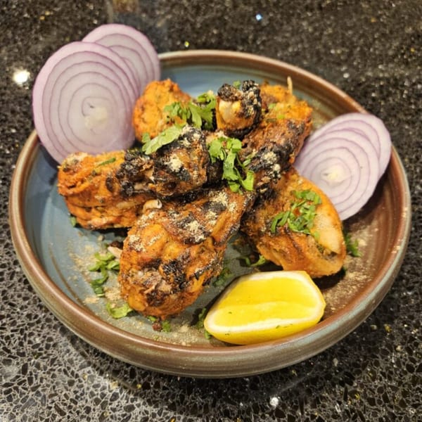 Mausam Indian Flavors' Tandoori Chicken, garnished with cilantro, red onion, and a lemon wedge.