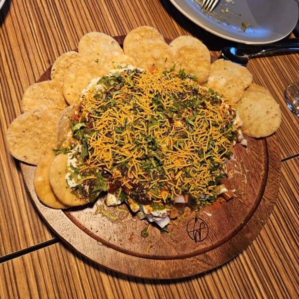 A large platter of Indian chaat, topped with sev and herbs, surrounded by crispy flatbreads.