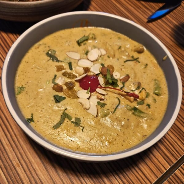 A bowl of creamy Indian curry, garnished with nuts, raisins, and a red cherry.