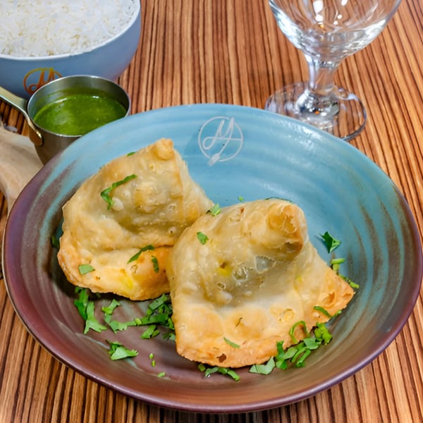 Two golden-brown samosas garnished with fresh cilantro on a blue and brown plate, with rice and chutney.