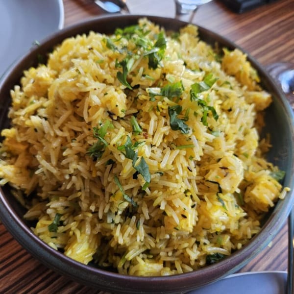 Close-up of a bowl of yellow Indian rice pilaf with paneer and fresh green herbs.