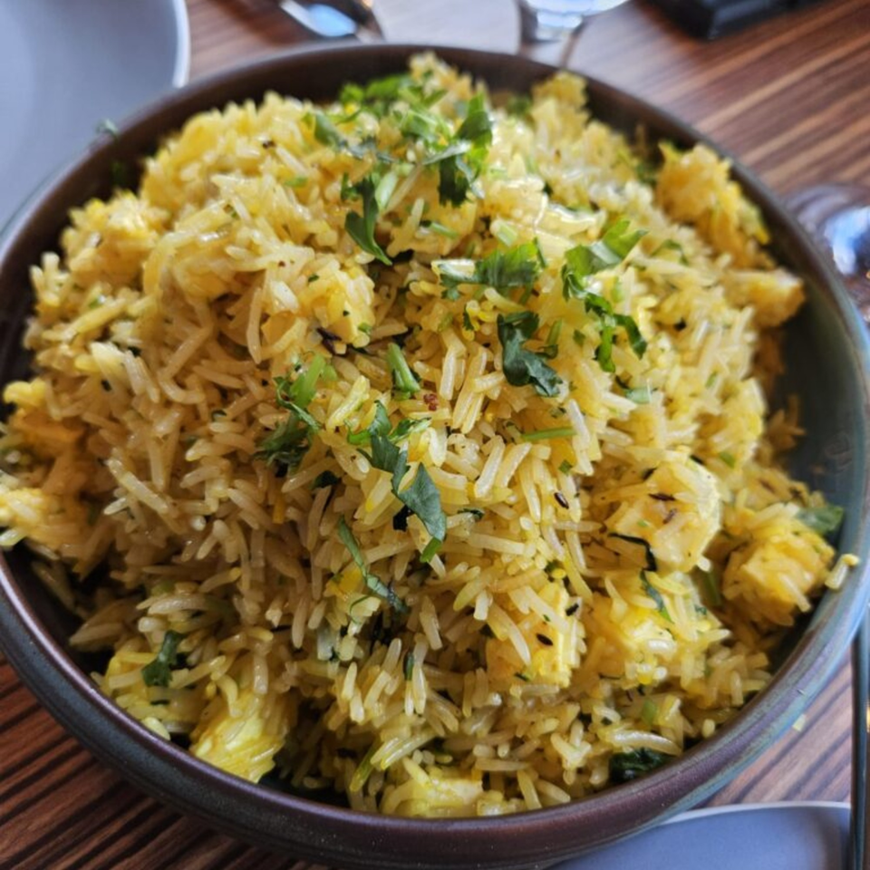 Close-up of a bowl of yellow Indian rice pilaf with paneer and fresh green herbs.