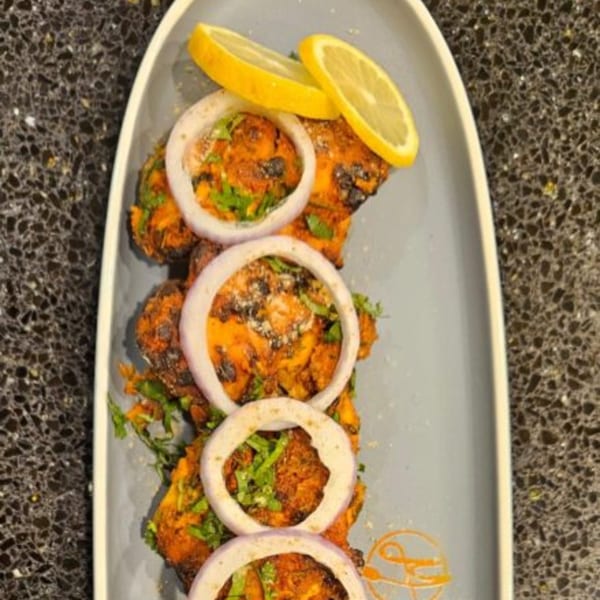 Mausam Indian Flavors' chicken tikka, garnished with onion rings, cilantro, and lemon slices.
