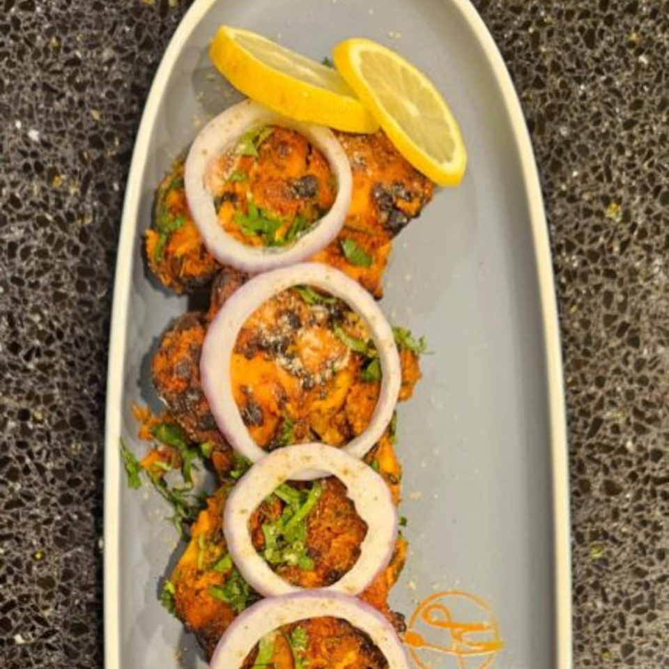 Mausam Indian Flavors' chicken tikka, garnished with onion rings, cilantro, and lemon slices.