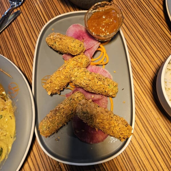 Crispy Indian appetizers, possibly cornflake-crusted, served with a side of chutney on a gray plate.