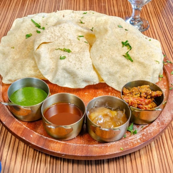 Papadum with four small bowls of chutneys and pickles on a wooden tray.