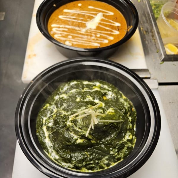 Two black bowls of Indian food, one with orange curry and the other with green spinach, on a counter.