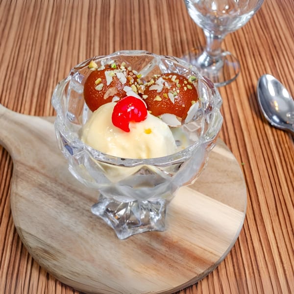 Gulab Jamun with vanilla ice cream and a cherry in a crystal bowl on a wooden board.