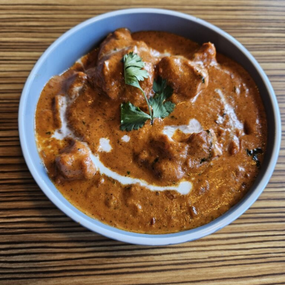 Mausam Indian Flavors' butter chicken, a rich orange curry with chicken pieces, cream swirls, and cilantro.